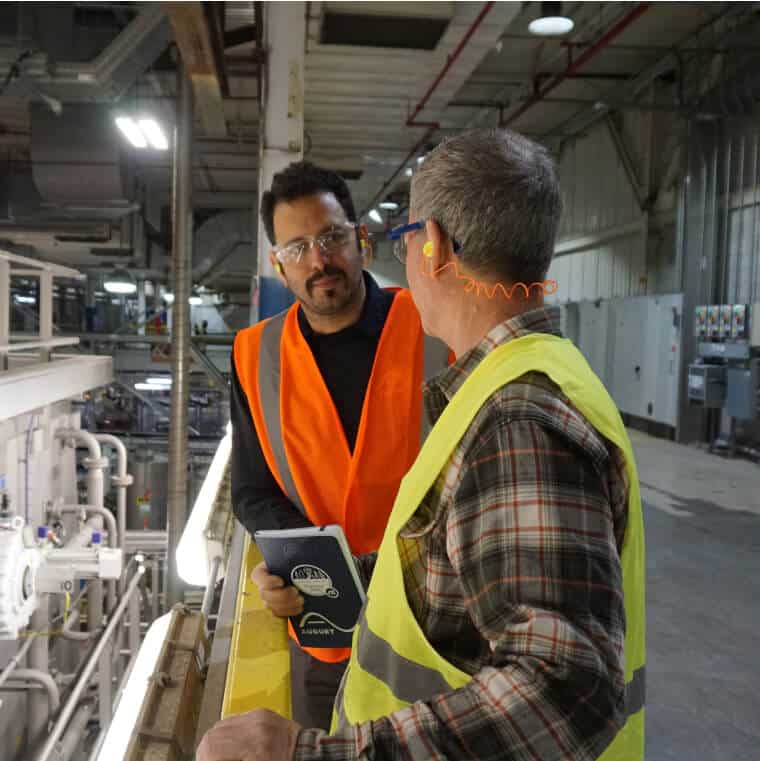 Two men standing in a factory talking to each other on the homepage.