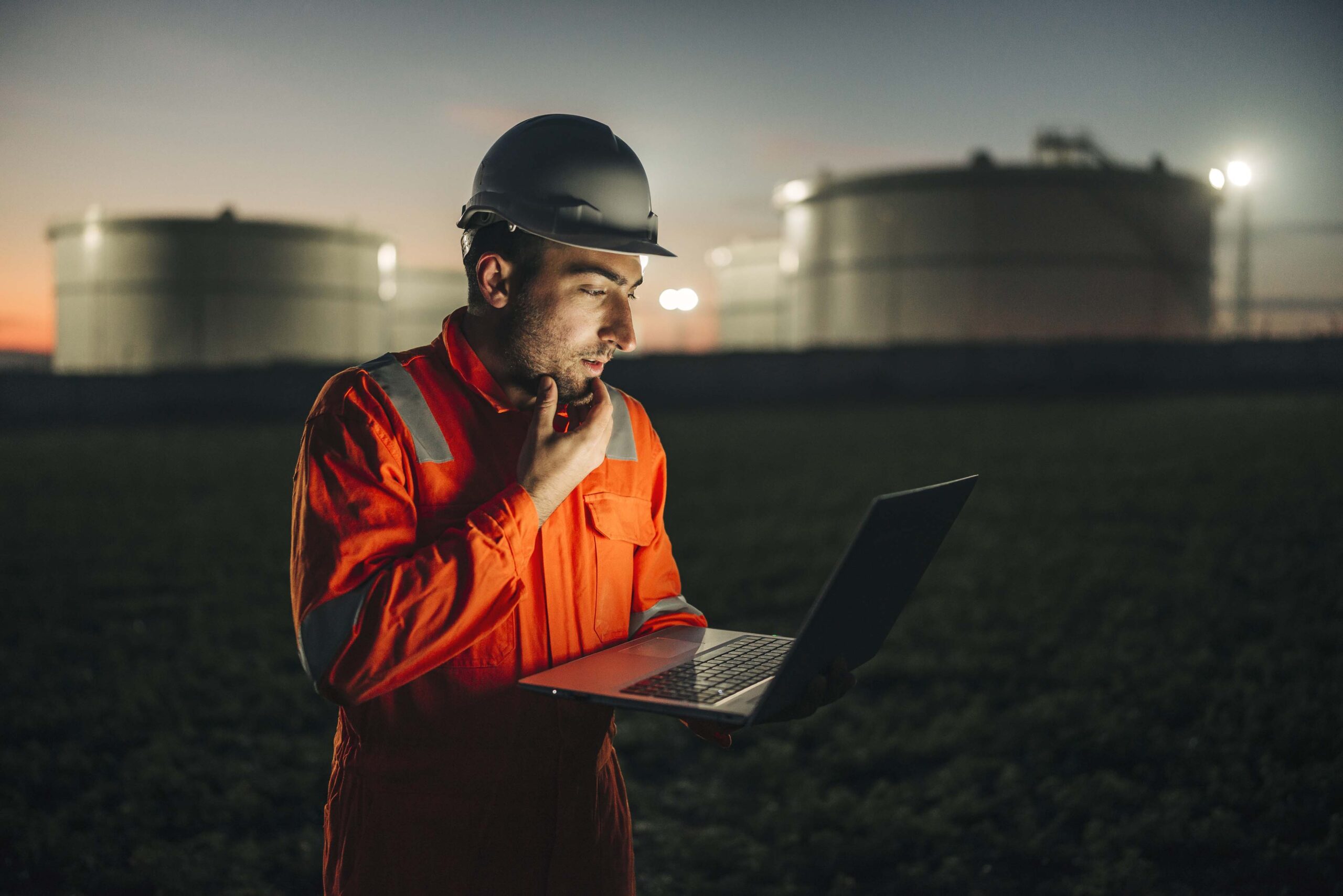 Man using laptop in front of oil refinery