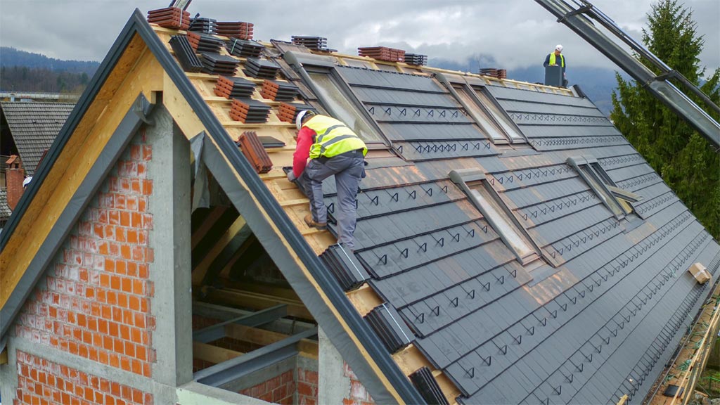 A man, an Analytics Systems Engineer, is working on the roof of a house belonging to America's Largest Roofing Manufacturer.