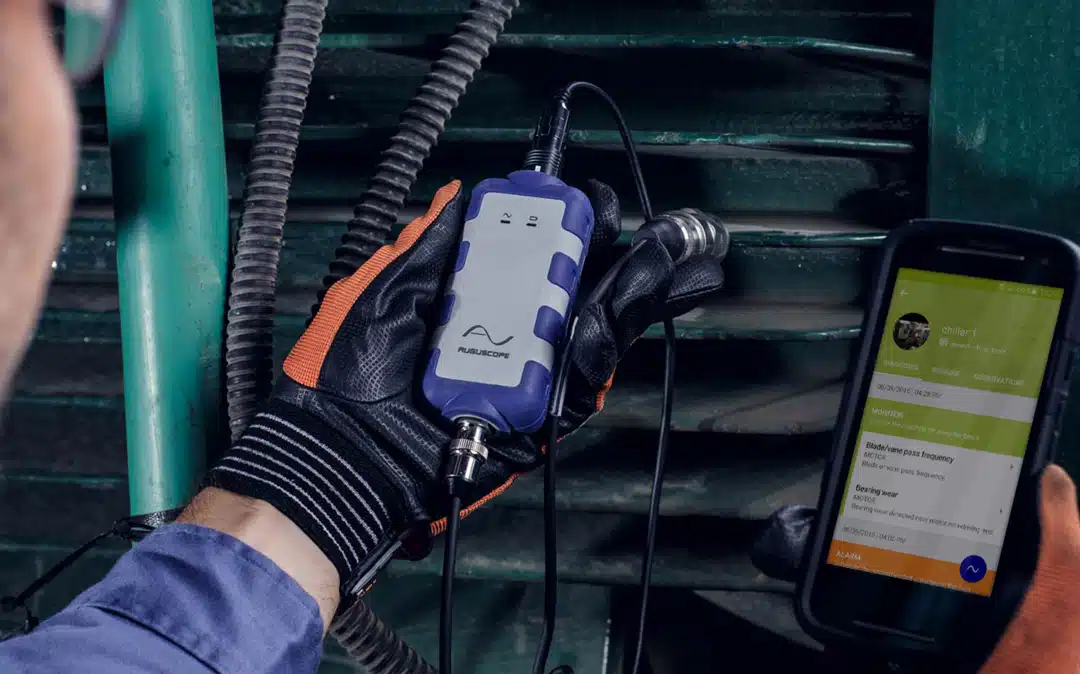 A worker is using a cell phone to check a machine for potential issues.