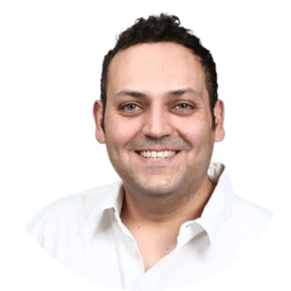 A man with short dark hair smiling, wearing a white collared shirt, against a plain light background.