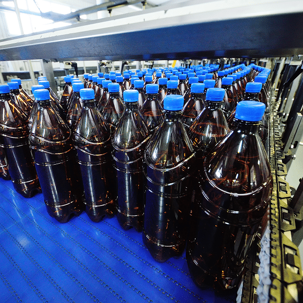 Rows of large plastic bottles with blue caps move along a conveyor belt inside a modern beverage manufacturing facility.