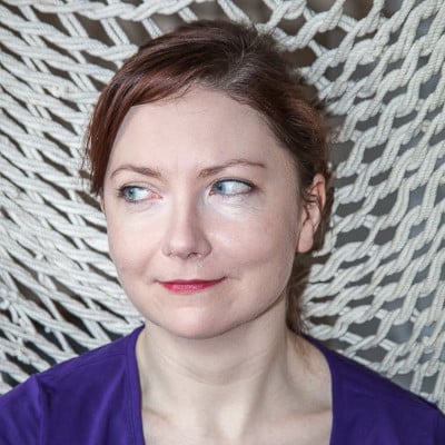 A woman with light skin and brown hair, wearing a purple top, looks to the side while seated against a white, woven rope background—a serene scene amidst the advancements of Industry 4.0.