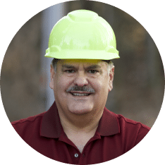 A man wearing a bright yellow hard hat and a red collared shirt, smiling at the camera, exudes confidence in crisis management.