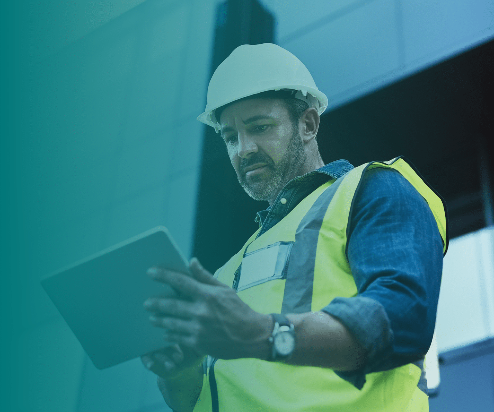 A construction worker wearing a hard hat and yellow safety vest looks at a tablet device, standing in front of a modern building.