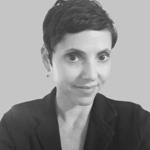 A woman with short dark hair wearing a dark blazer is looking at the camera against a plain background, embodying the commitment to Net Zero initiatives.