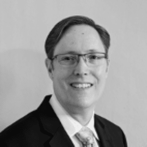 Black and white photo of a person in a suit, wearing glasses, smiling at the camera—projecting confidence and commitment to achieving Net Zero goals.