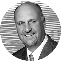 Black and white headshot of a man in a suit and tie, smiling at the camera with a blurred background featuring horizontal lines, showcasing the professionalism of an Accenture executive.