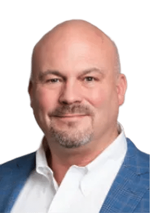 A middle-aged man with a bald head and goatee, wearing a white shirt and a blue plaid blazer, smiling at the camera against a plain light background.