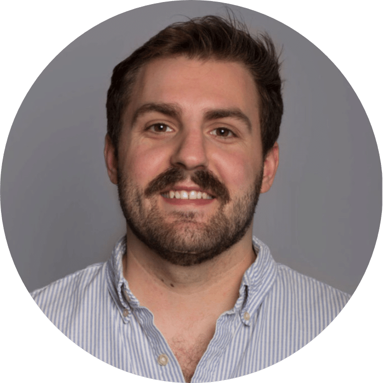 A person with short hair and a beard, wearing a light blue and white striped button-up shirt, smiles for a portrait against a gray background, embodying the essence of Preventive Maintenance.