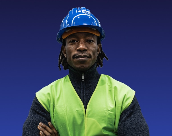 A man wearing a blue safety helmet and a neon green safety vest stands with his arms crossed against a solid dark blue background.