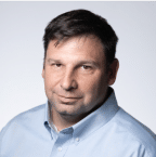 A middle-aged man with short dark hair, wearing a light blue collared shirt, is looking directly at the camera against a plain background, his expression reflecting his commitment to improved reliability in machine health within the pulp and paper industry.