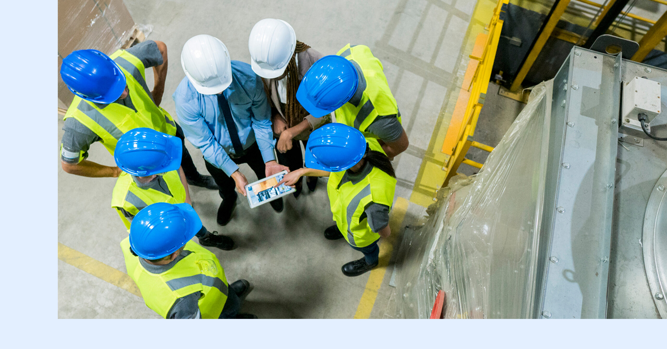 A maintenance team in hard hats and safety vests gathers around a tablet on a plant floor to review equipment data.