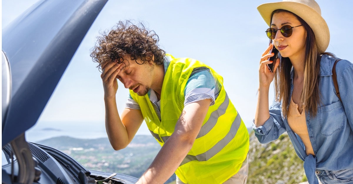 A man in a reflective vest checks under hood while partner calls for help.