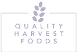 Logo for Quality Harvest Foods featuring purple leaves arranged in a vertical cluster above the company name, which is written in uppercase letters and spaced out evenly on a white background.