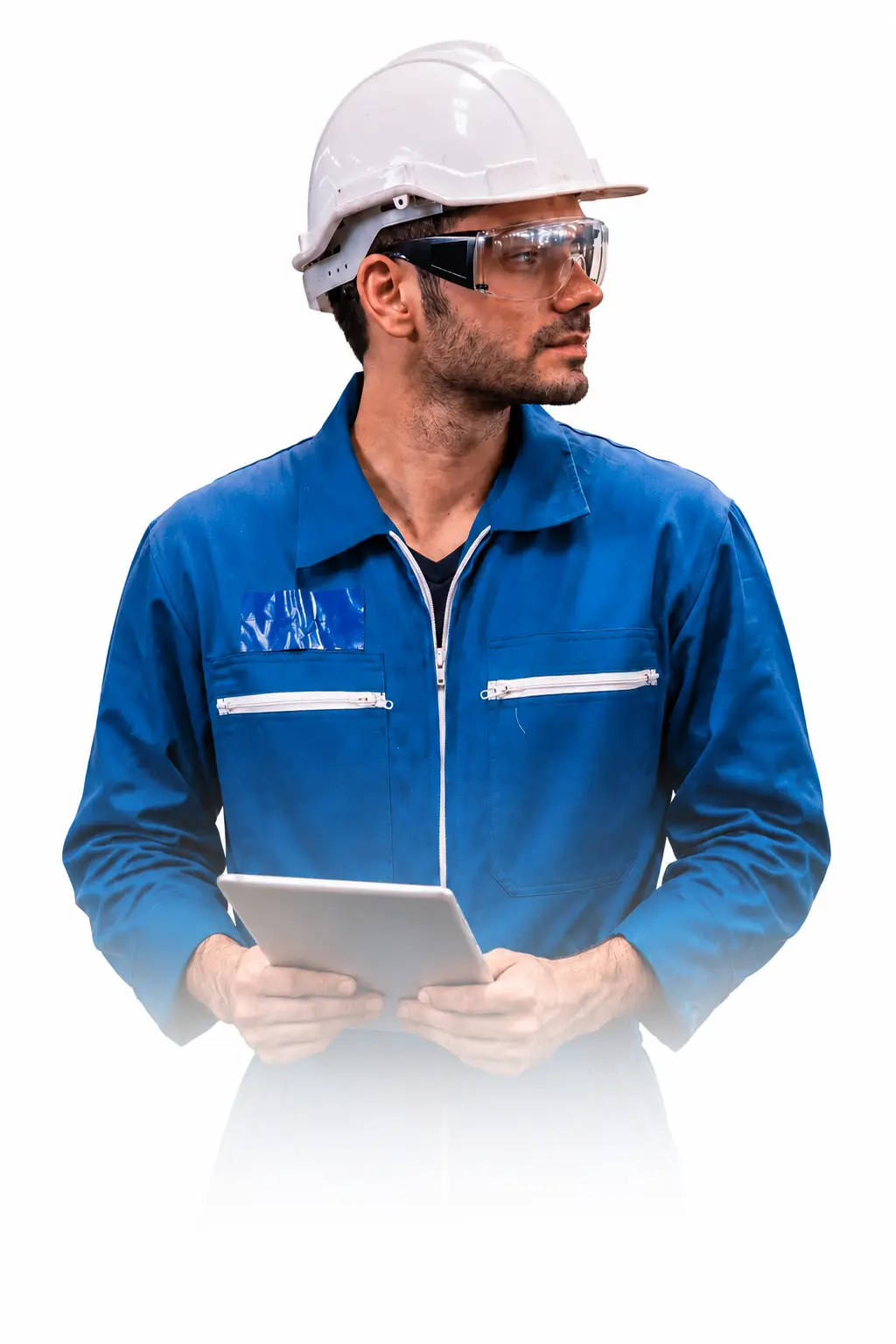 A man wearing a blue coverall, white safety helmet, and protective glasses holds a tablet and looks to the side, appearing to be an engineer or construction worker.